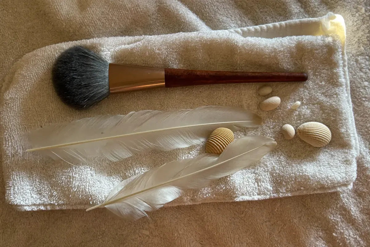 A soft brush, white feathers and small seashells on a folded towel