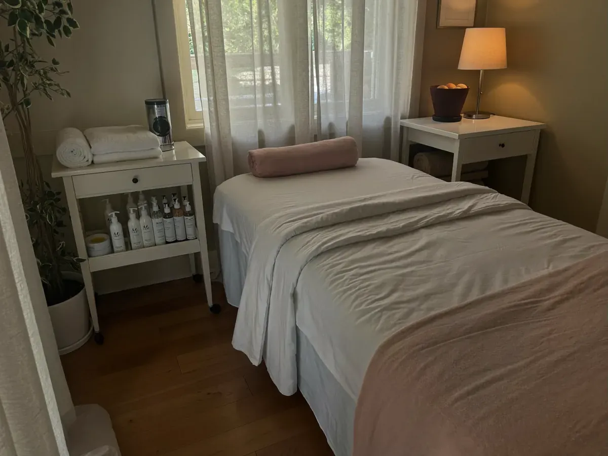 A calm treatment room with a spa bed made up in white and blush